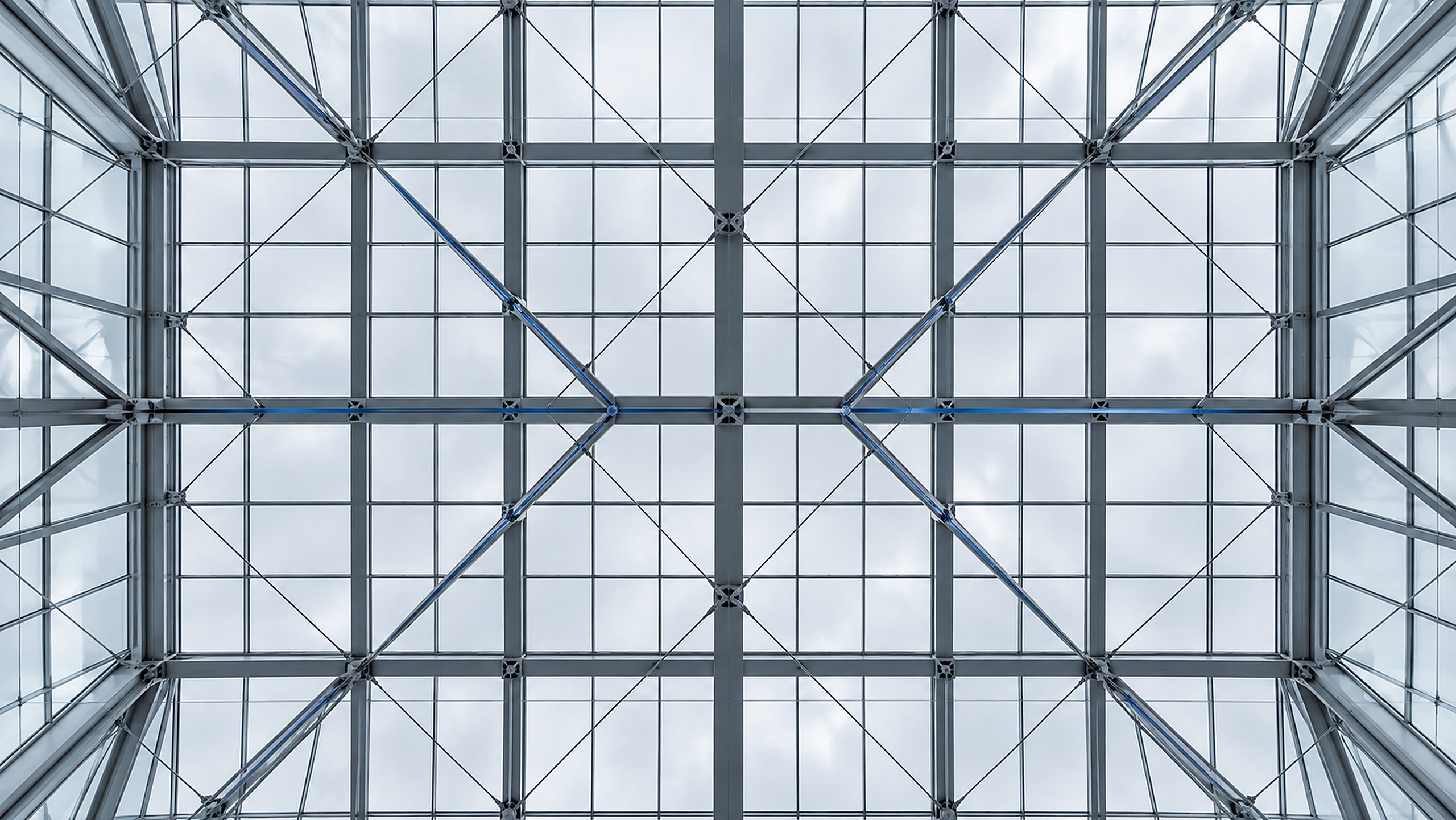 A steel and glass atrium roof seen from directly below, its beams forming a precise lattice